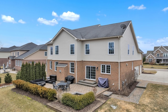 back of property featuring concrete driveway, brick siding, a patio, and an attached garage