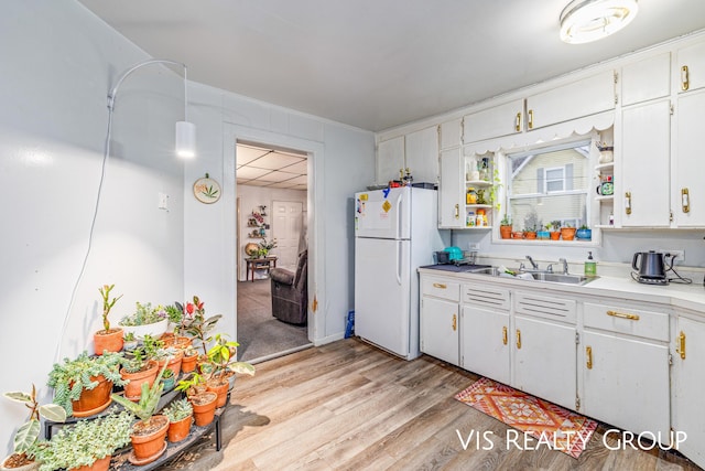 kitchen with light countertops, light wood-style floors, freestanding refrigerator, white cabinetry, and a sink