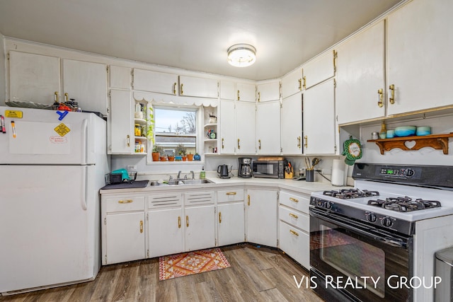 kitchen with gas range, a sink, freestanding refrigerator, and white cabinets