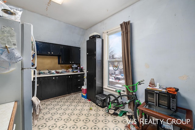 kitchen with freestanding refrigerator, vaulted ceiling, light countertops, dark cabinetry, and a sink