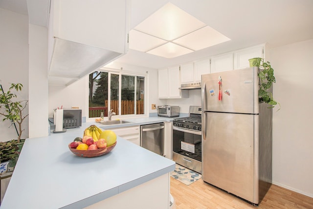 kitchen featuring light wood-style flooring, appliances with stainless steel finishes, under cabinet range hood, white cabinetry, and a sink