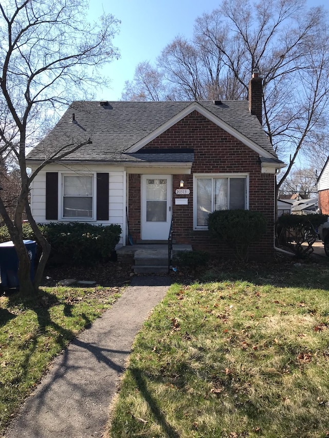 bungalow-style house with a shingled roof, a front yard, brick siding, and a chimney