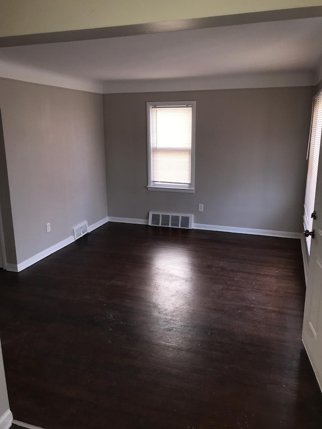 empty room featuring baseboards, visible vents, and dark wood-style flooring