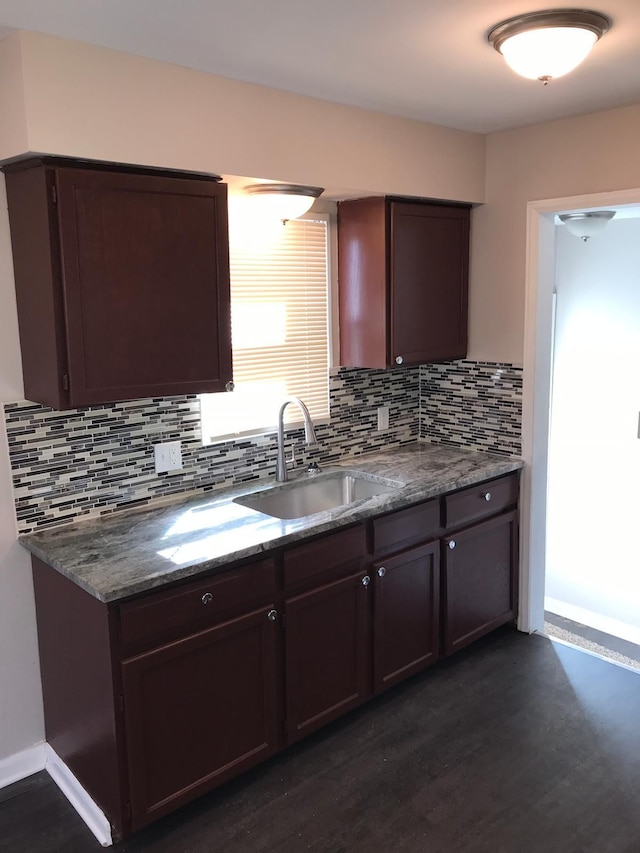 kitchen with tasteful backsplash, dark wood-type flooring, a sink, dark stone countertops, and dark brown cabinets