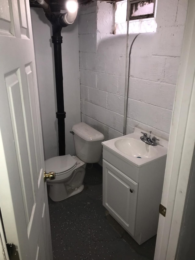 half bathroom featuring concrete block wall, vanity, and toilet