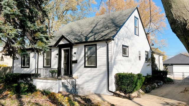 view of front facade featuring a shingled roof, an outbuilding, fence, and a garage