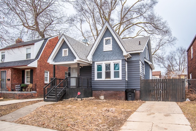 view of front facade featuring covered porch, a shingled roof, a gate, and fence