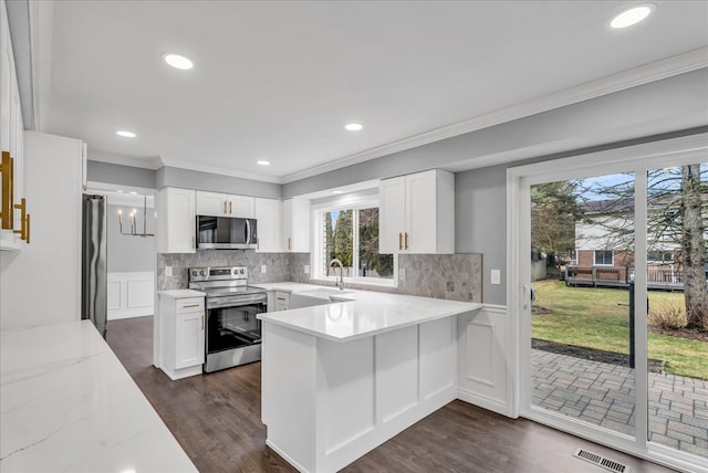 kitchen featuring a peninsula, a sink, visible vents, ornamental molding, and appliances with stainless steel finishes