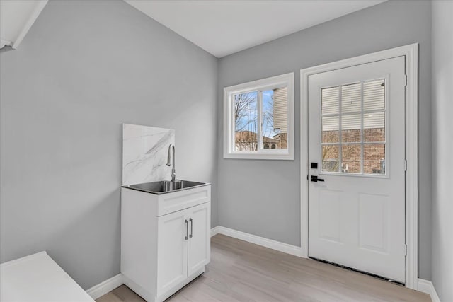 doorway to outside featuring light wood-style flooring, baseboards, and a sink