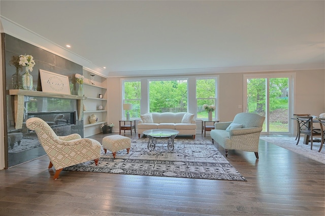 living area featuring built in features, wood-type flooring, ornamental molding, and a tiled fireplace