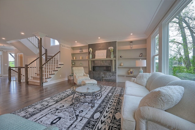 living area with stairs, a fireplace, ornamental molding, and wood finished floors