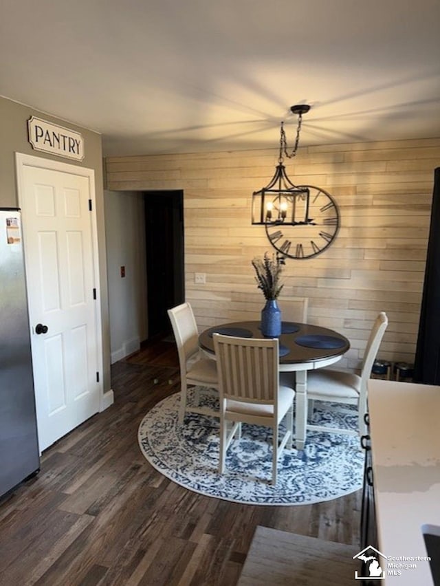 dining space with dark wood-style floors, wooden walls, and baseboards