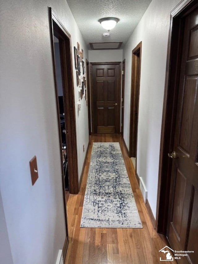 corridor featuring visible vents, baseboards, a textured ceiling, and light wood finished floors