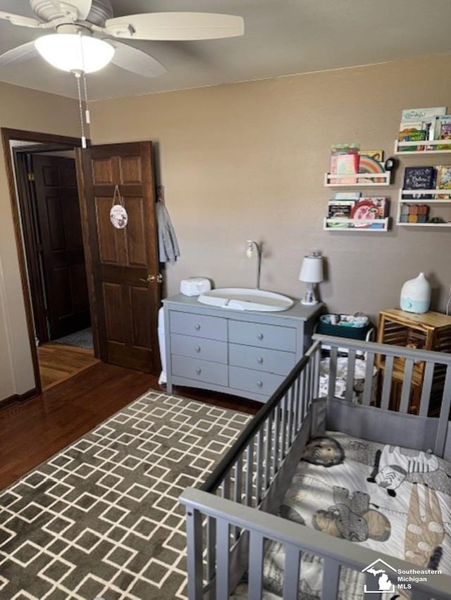 bedroom with a ceiling fan, a nursery area, and wood finished floors