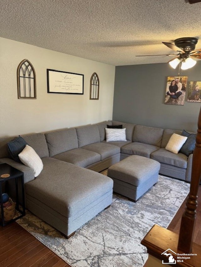 living area with a textured ceiling, a ceiling fan, and dark wood-style flooring