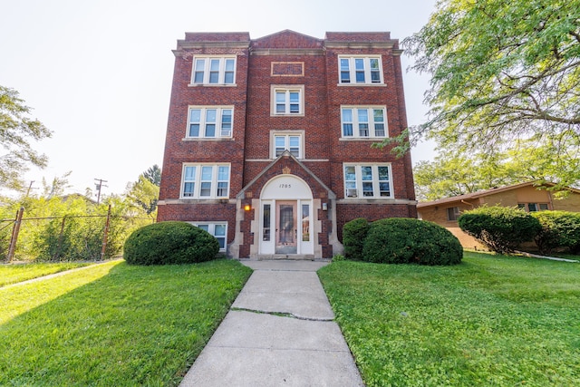 view of front facade with brick siding, a front lawn, and fence