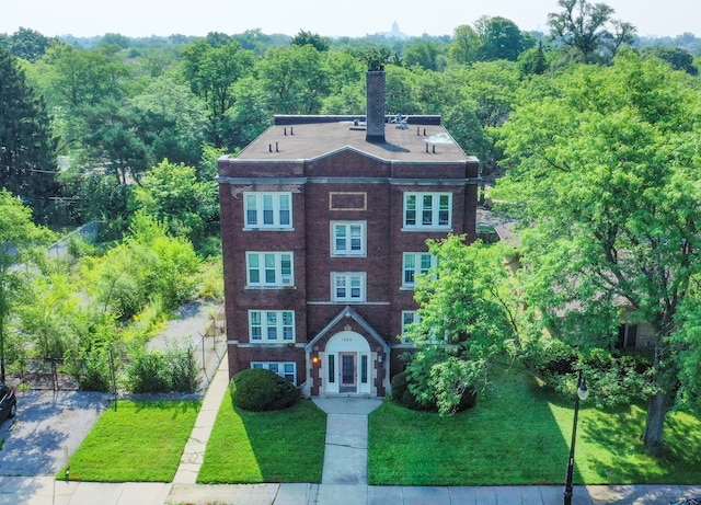 view of front of property with fence, a wooded view, a front yard, brick siding, and a chimney