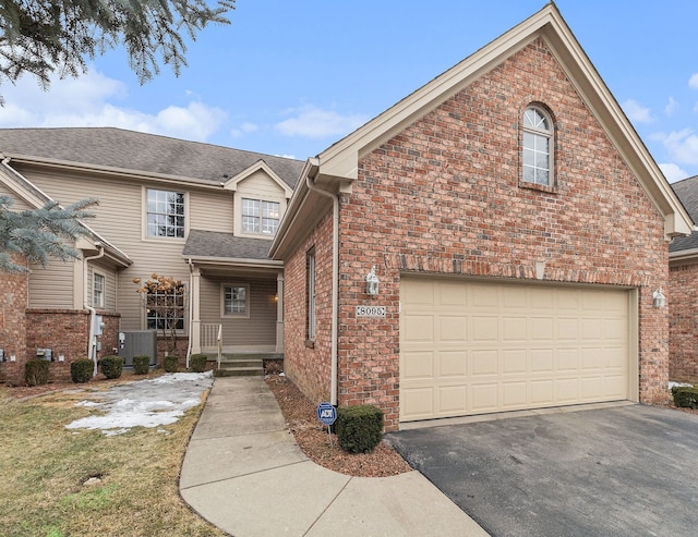 view of front facade with a garage, central AC, brick siding, and driveway