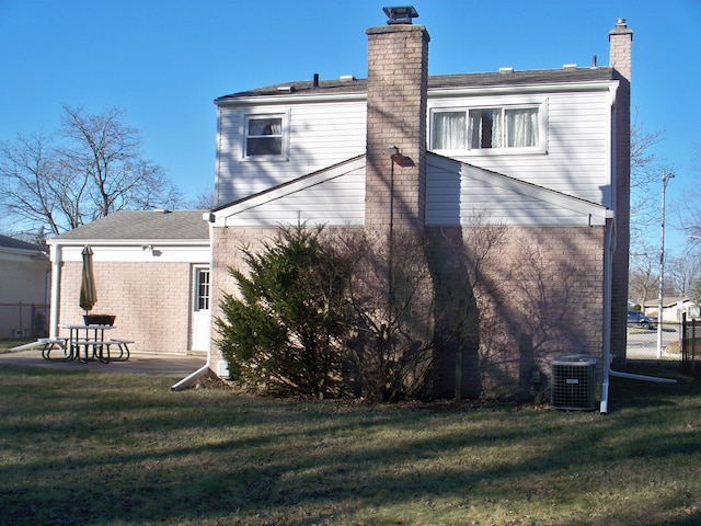 back of house featuring central AC, a yard, a chimney, and brick siding