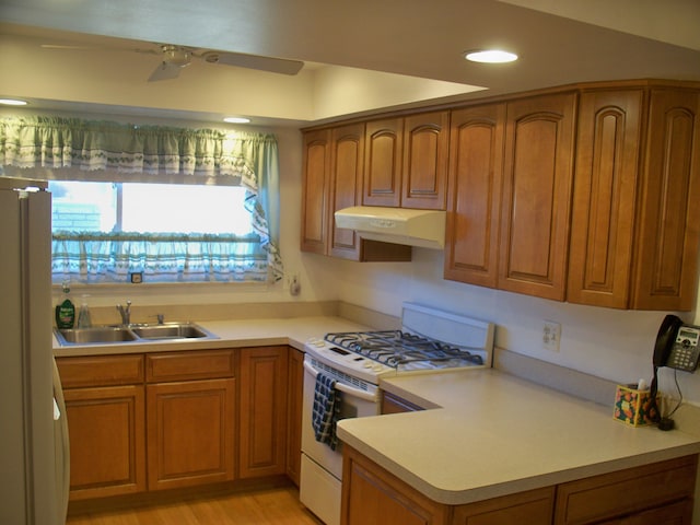 kitchen with white appliances, under cabinet range hood, brown cabinetry, and a sink