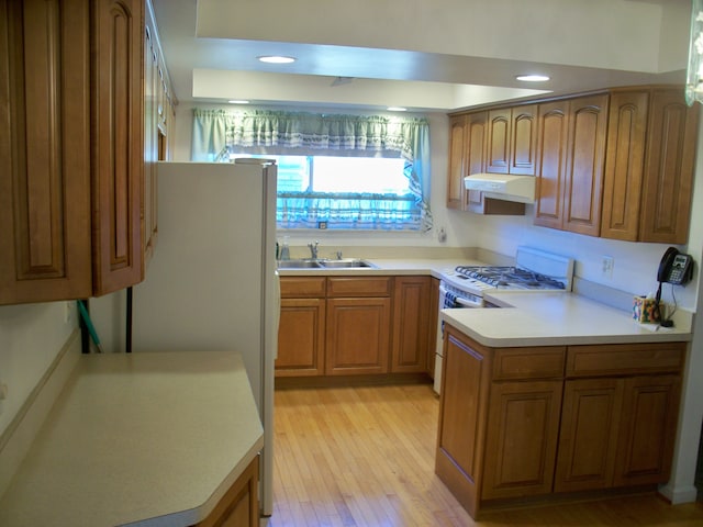 kitchen featuring brown cabinets, light countertops, a sink, white appliances, and under cabinet range hood