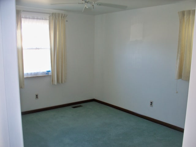 carpeted spare room featuring a ceiling fan, visible vents, and baseboards