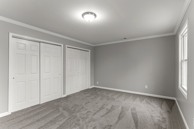 unfurnished bedroom with carpet floors, crown molding, visible vents, and two closets