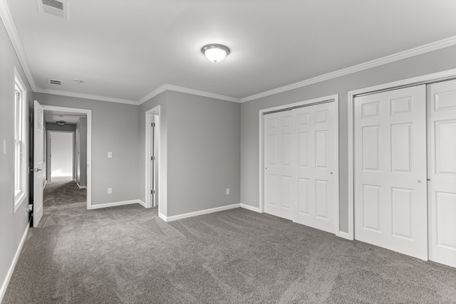 unfurnished bedroom featuring carpet floors, crown molding, visible vents, and multiple closets