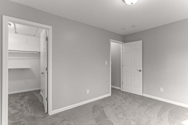 unfurnished bedroom featuring attic access, carpet, a spacious closet, and baseboards