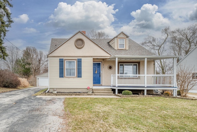 view of front facade featuring an outbuilding, stucco siding, a shingled roof, covered porch, and a front lawn