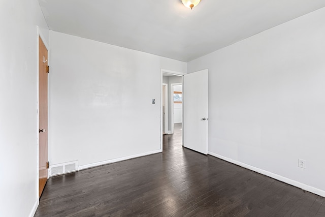 spare room featuring dark wood-type flooring, visible vents, and baseboards