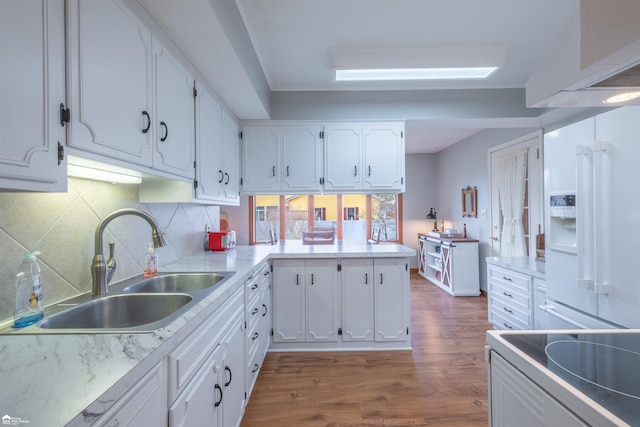 kitchen featuring white appliances, wood finished floors, a sink, white cabinetry, and backsplash