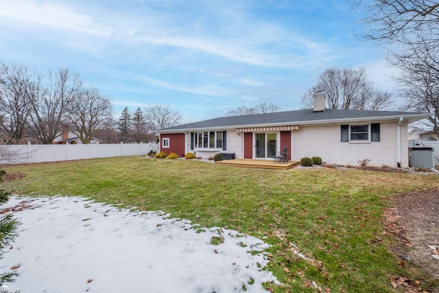 single story home featuring brick siding, a chimney, a front yard, fence, and a wooden deck