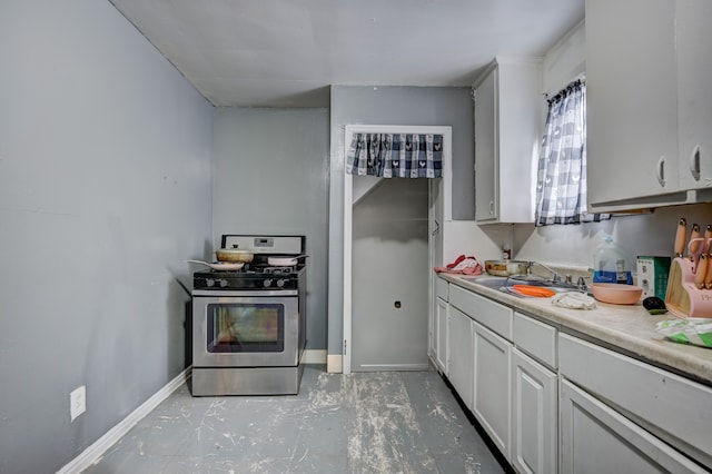 kitchen with a sink, white cabinetry, light countertops, baseboards, and stainless steel gas range