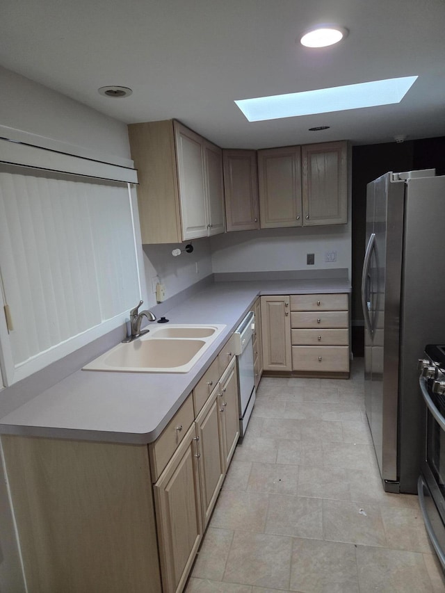 kitchen with a skylight, light countertops, stainless steel appliances, light brown cabinetry, and a sink