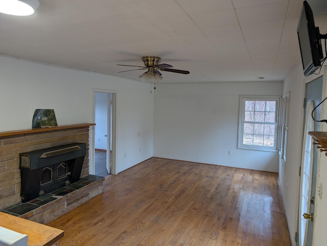 unfurnished living room with wood finished floors, a wood stove, and a ceiling fan