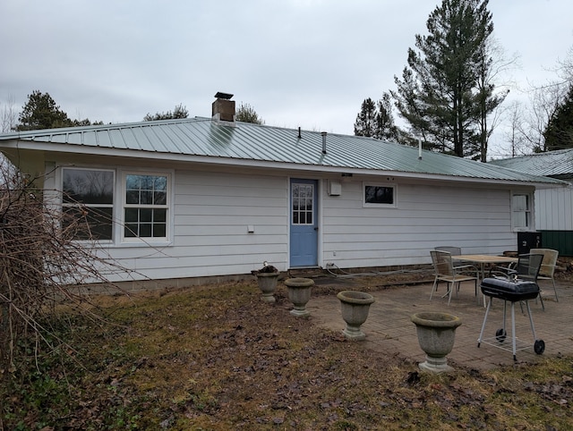 rear view of house featuring a patio area, metal roof, and a chimney