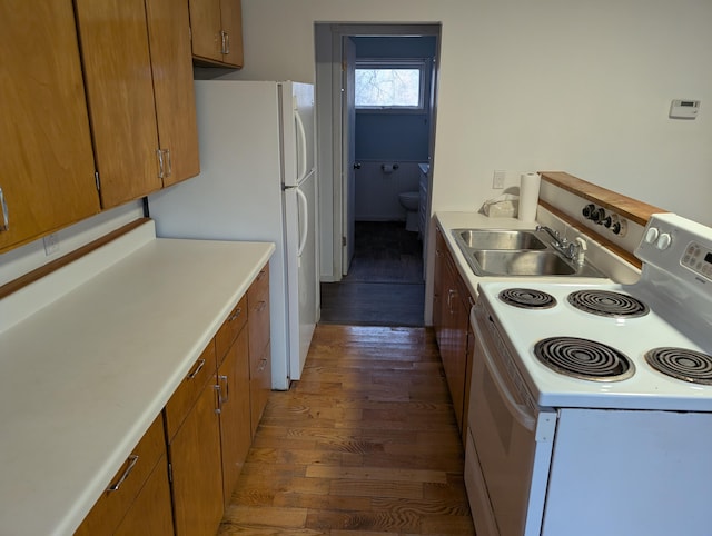 kitchen with white appliances, brown cabinetry, dark wood-style floors, light countertops, and a sink