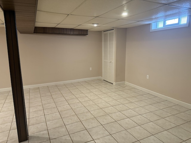 basement with a paneled ceiling and baseboards