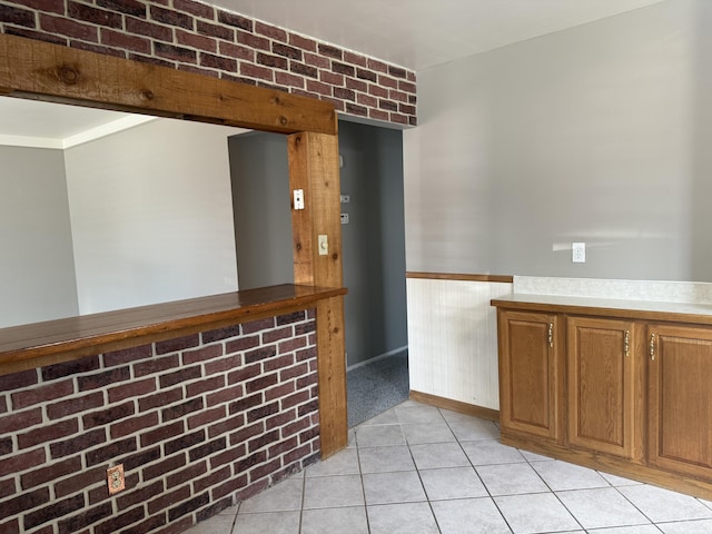 kitchen featuring a wainscoted wall, light countertops, light tile patterned flooring, and brown cabinets