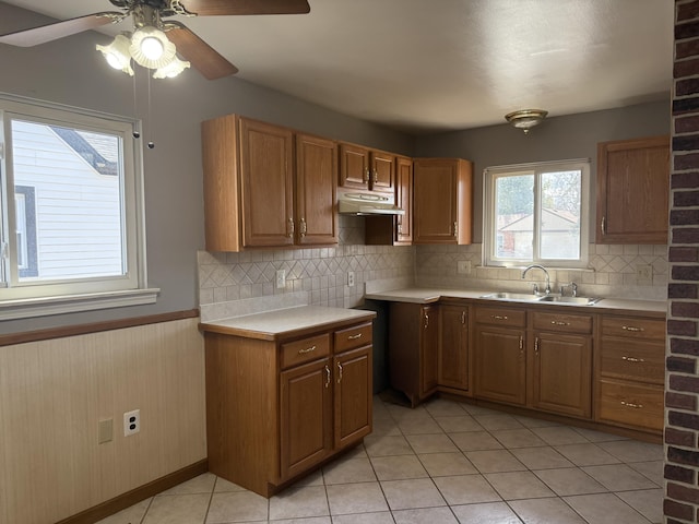 kitchen featuring brown cabinetry, a wainscoted wall, light countertops, under cabinet range hood, and a sink