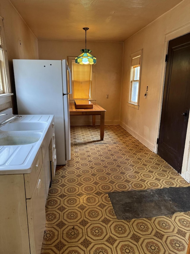 kitchen featuring light tile patterned floors, hanging light fixtures, freestanding refrigerator, and baseboards