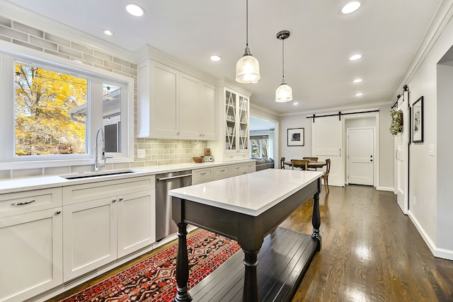 kitchen with a sink, crown molding, stainless steel dishwasher, a barn door, and backsplash