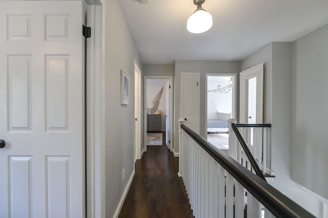 hall featuring baseboards, an upstairs landing, and dark wood-style flooring