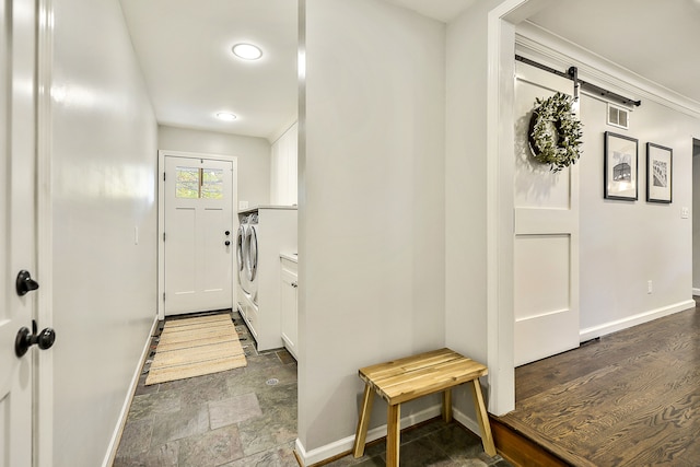 laundry area featuring a barn door, visible vents, baseboards, and stone finish flooring