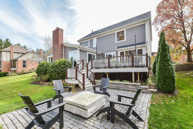 back of property featuring a fire pit, a wooden deck, a lawn, a chimney, and a patio area