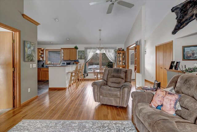 living area with ceiling fan, light wood-style floors, baseboards, and high vaulted ceiling