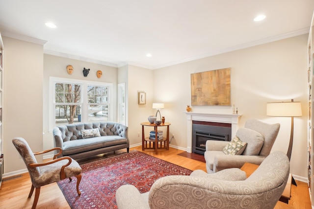 living area featuring recessed lighting, wood finished floors, a fireplace with flush hearth, baseboards, and ornamental molding