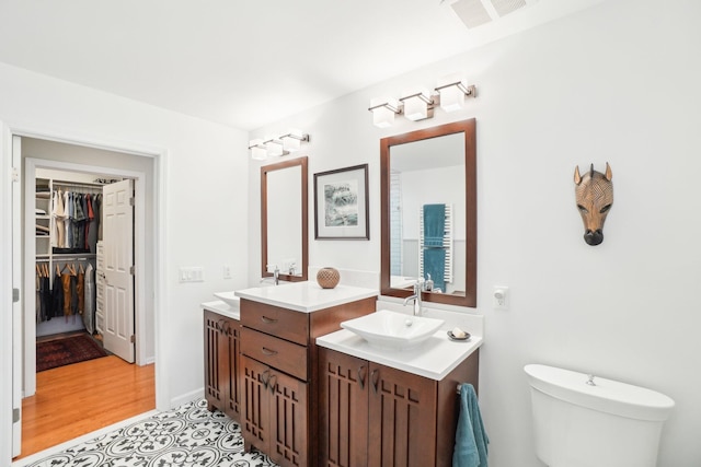 full bath featuring two vanities, visible vents, a sink, and toilet