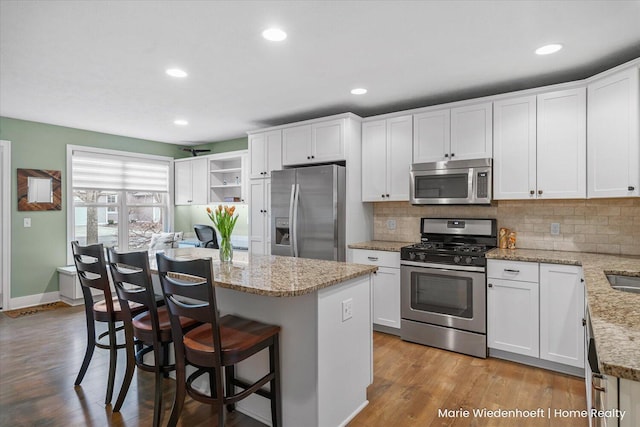 kitchen with stainless steel appliances, a kitchen island, backsplash, and wood finished floors